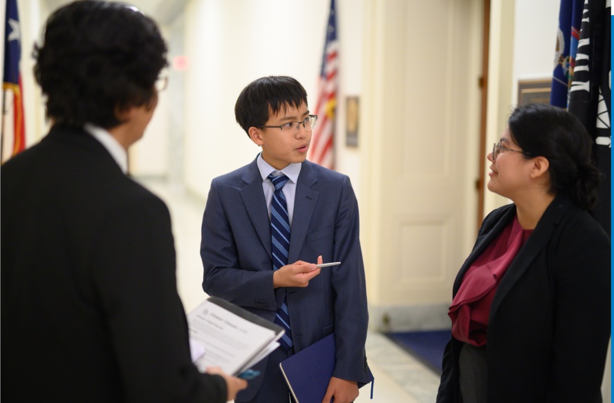 Three young people dressed formally, engaged in conversation in what seems to be a government building.