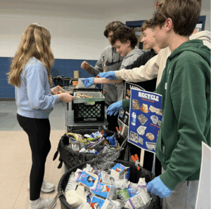 students helping each other divide up leftover lunch into receptacles